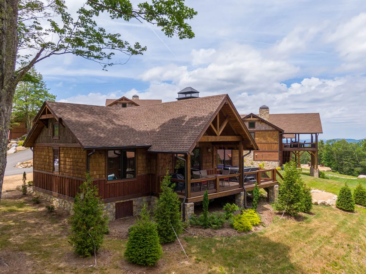 An exterior view of the property featuring a spacious wooden porch area set against a backdrop of lush greenery and distant mountains. The porch offers ample room for outdoor lounging and is surrounded by natural beauty, suggesting easy access to nearby trails and open spaces ideal for exploring with pets.