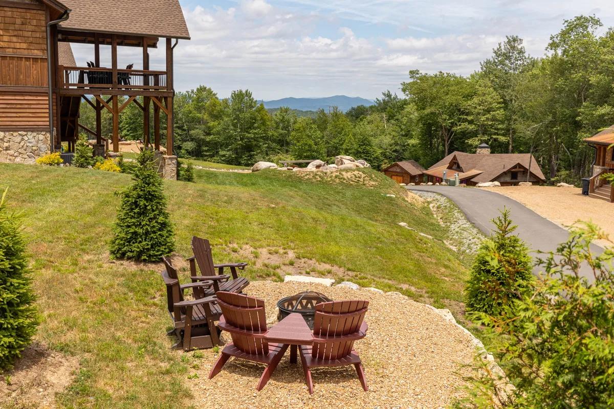 An inviting outdoor setting with Adirondack chairs encircling a fire pit, overlooking expansive mountain views. The area is designed for gathering, with ample space for friends or family to enjoy an evening by the fire while surrounded by natural scenery.
