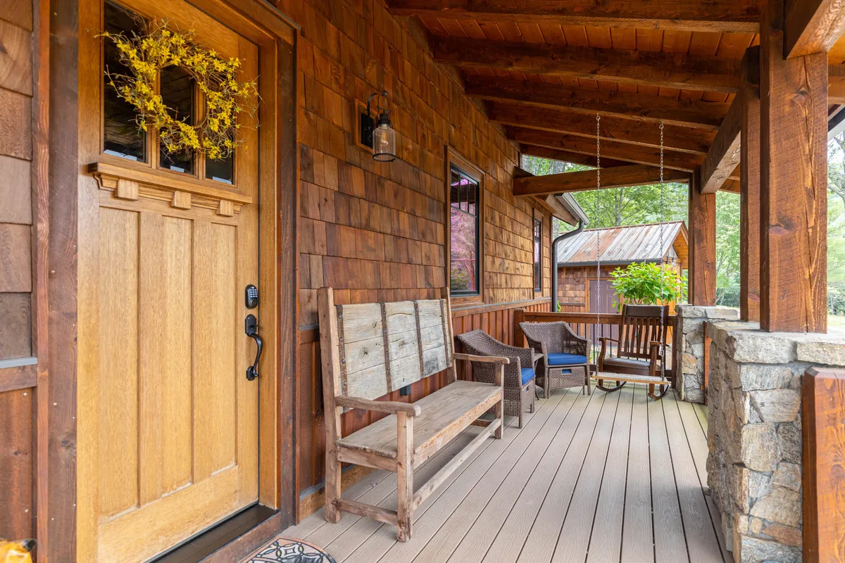 A cozy front porch scene with a wooden door adorned by a decorative wreath, bench seating, stone walls, and atmospheric hanging lights. The inviting entryway is surrounded by greenery, hinting at the welcoming environment awaiting both guests and their pets.