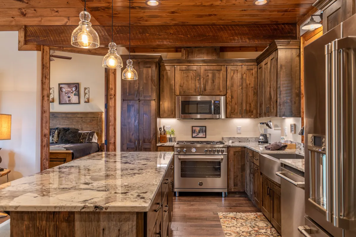 This image centers on a modern kitchen with gleaming granite countertops, warm wooden cabinetry, stylish hanging light fixtures, and high-end kitchen appliances. The space is arranged for cooking, entertaining, and casual family gatherings, radiating a warm and inviting atmosphere.