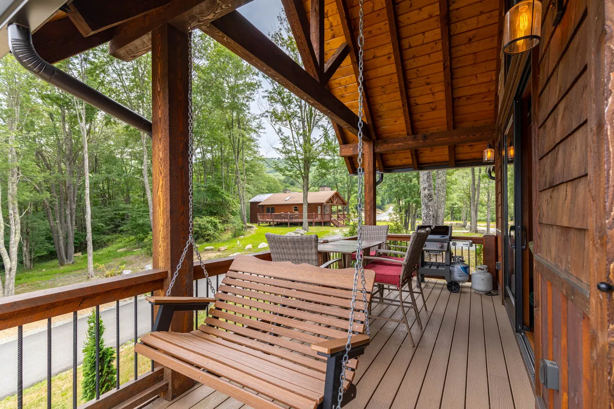 A tranquil outdoor area featuring a swinging bench, a dining set, and mature trees providing shade. This space evokes a relaxed atmosphere for socializing, dining, or simply enjoying the fresh mountain air alongside pets.