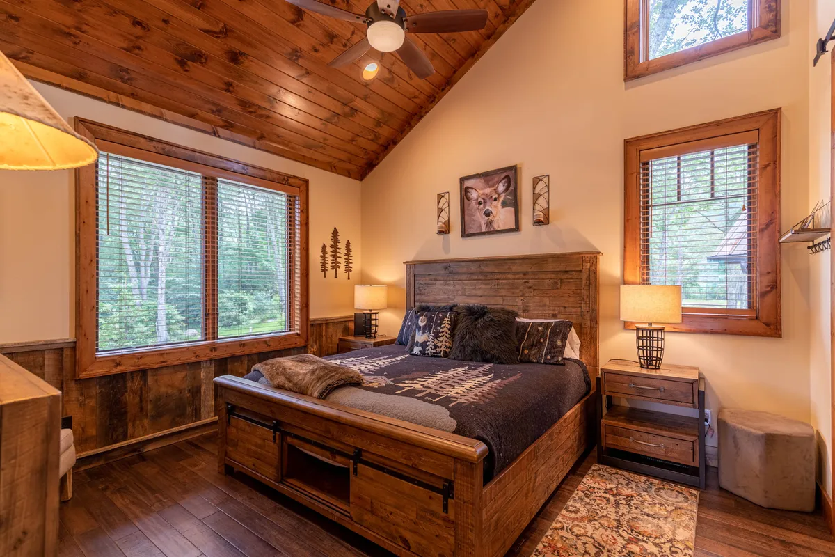A cozy king bedroom featuring a wooden bed frame with decorative pillows, a side table and lamp, and a window providing natural light and a view of the outdoors. The space exudes tranquility and warmth—perfect for unwinding after a busy day.