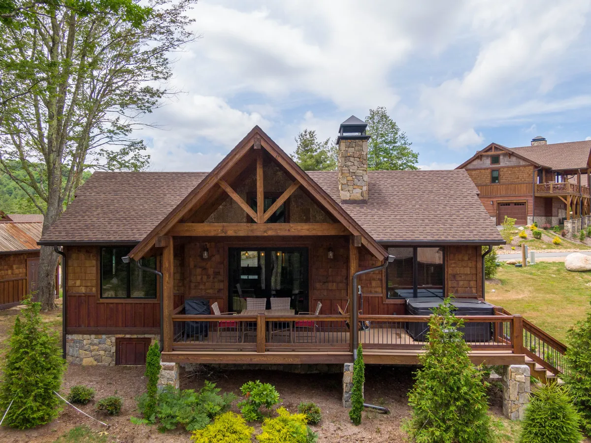 A wide view of the wooden deck with a stone chimney, large windows, and lush surrounding greenery. The deck offers space for outdoor gatherings, morning coffee, or grilling, and the home's architecture blends harmoniously with the mountain landscape.